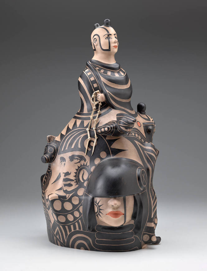 Ceramic sculpture depicting a male bust at the top, with seven faces below, decorated in black and muted red-orange paint against a light beige base.