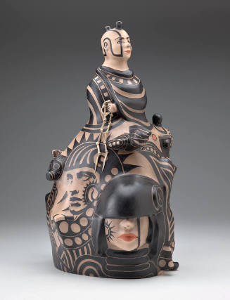 Ceramic sculpture depicting a male bust at the top, with seven faces below, decorated in black and muted red-orange paint against a light beige base.
